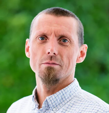 Photo of Fil McIntyre, wearing a checked shirt, against a green outdoor background.